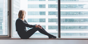 woman sitting in large window of office building - psychological aspect of recovery
