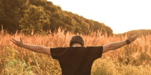 young man in field with head bowed and arms open to the sky - spiritual aspect of recovery