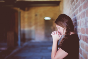 woman with braids leaning against brick building exterior praying - christian alcohol rehab