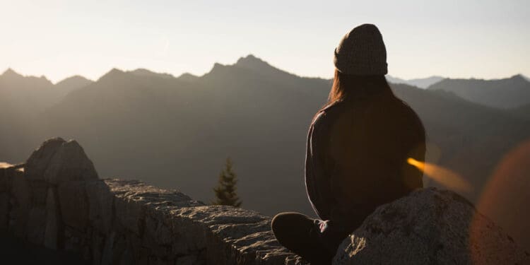 young woman sitting on cliff looking out over nature - recovery from addiction