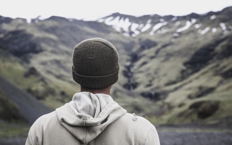 young man in sock cap and hooded sweatshirt facing away from camera and looking at mountain range - cognitive behavior therapy addiction
