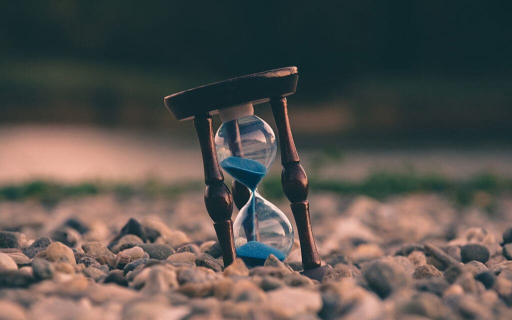 wooden hourglass with blue sand sitting in rocks