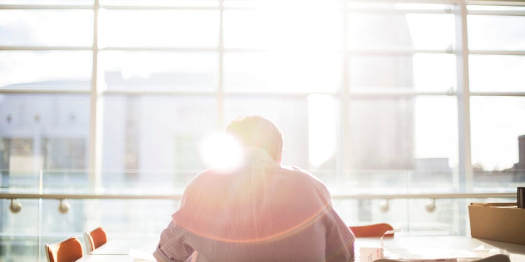 man sitting at work office facing large glass windows - back to work after rehab