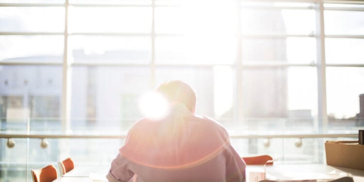 man sitting at work office facing large glass windows - back to work after rehab