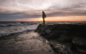person standing on rocky shore during sunset