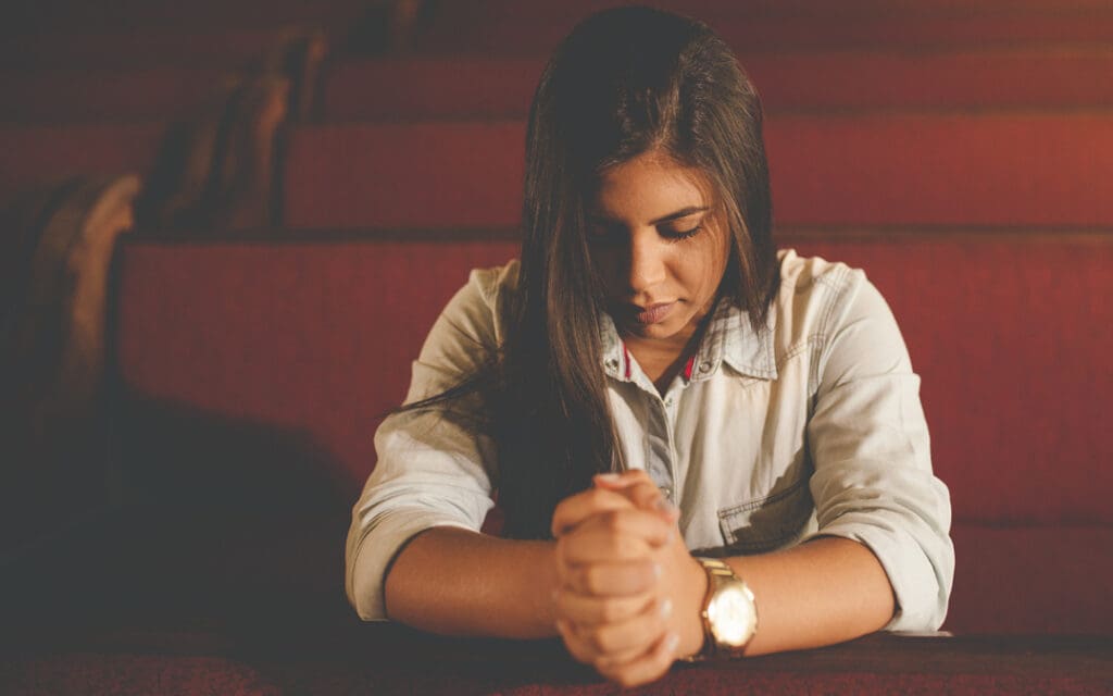 Can You Believe in God and Be Addicted to Drugs?, young brunette woman praying in a church pew