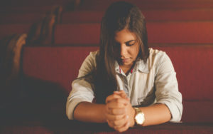 young brunette woman praying in a church pew