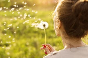 woman blowing dandelion seeds into wind