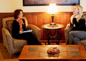 two cheerful women talking on chairs with table and lamp between them