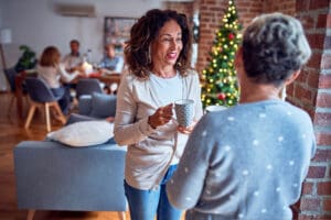 two women drinking coffee and talking at holiday gathering - the holidays