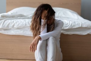 young woman sitting on floor at foot of bed with hand on head - stressed - withdrawal