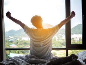 man waking up and stretching facing window - sleep