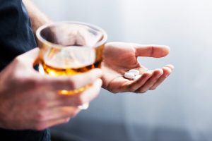 person holding glass of liquor in one hand and white pills in the other - alcohol and opioids