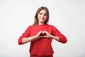 pretty young woman in red sweater making the shape of a heart over her heart