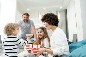 family of four smiling and opening up Valentine's presents together - two young children with parents - Valentine's Day