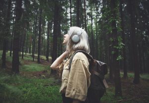 pretty young woman with platinum blonde hair listening to headphones while she walks in the woods - creativity and recovery