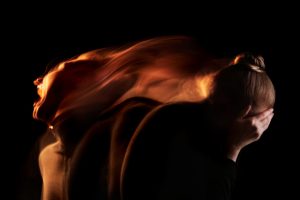 long exposure shot of young woman in distress - looks like fire against a dark background - co-occurring disorders