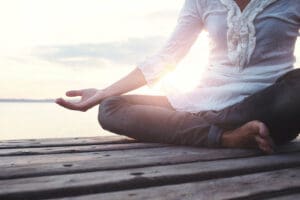 cropped shot of a woman sitting on a wooden pier meditating - meditation and recovery