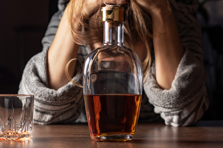 Female alcoholism. Female woman sit to table drink alcohol bottle at home sad alone alcoholism Signs and Symptoms rehab abuse and recovery problems
