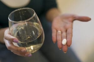 woman holding alcohol in one hand and a pill in the other - what drug is the hardest to quit?