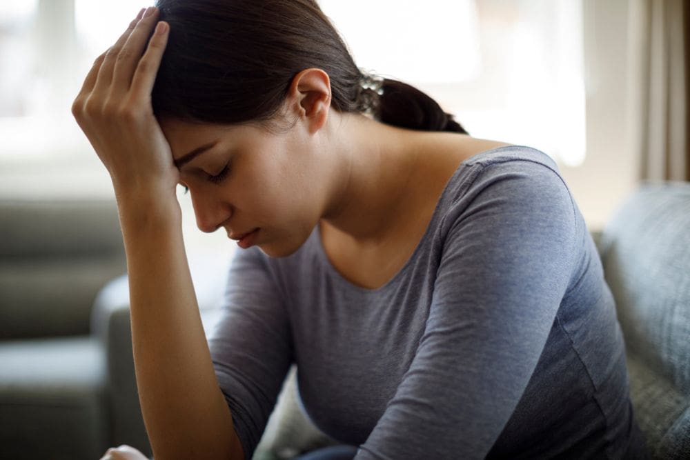 Woman sitting on a couch with her head resting on her hand, eyes closed.