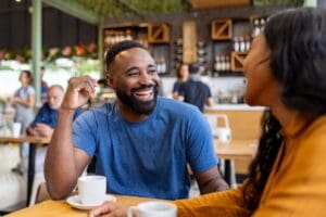 Smiling couple enjoying a conversation over coffee at a café, reflecting connection, comfort, and positive communication in a relationship.