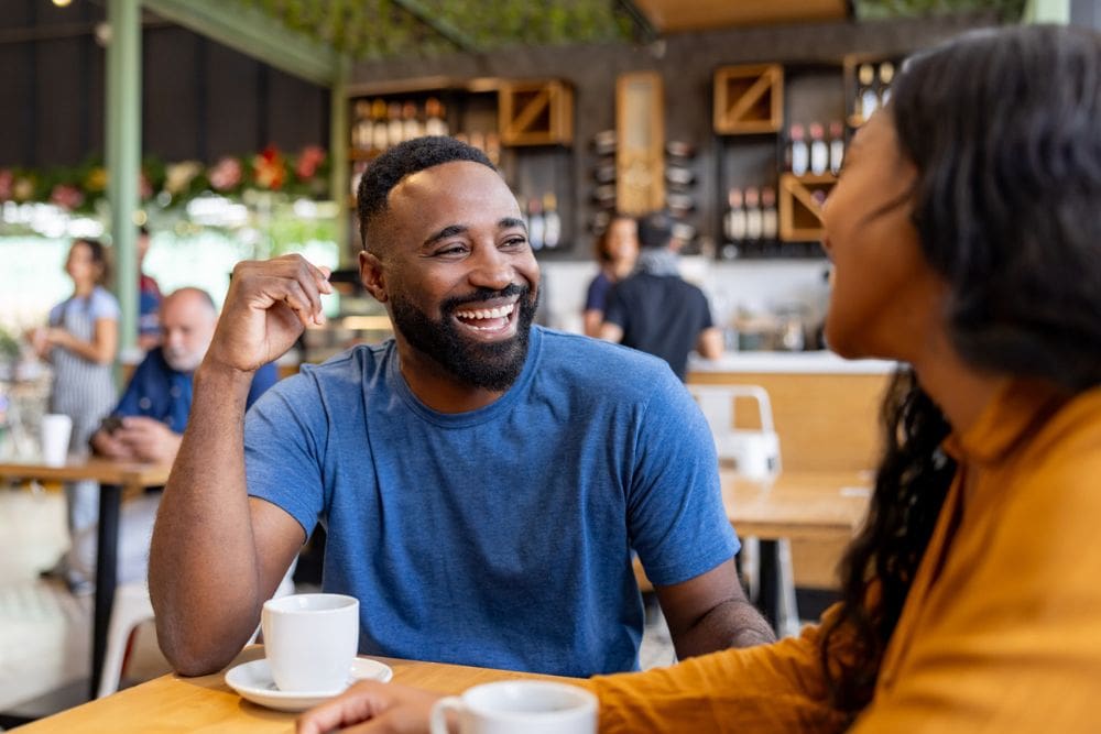 Smiling couple enjoying a conversation over coffee at a café, reflecting connection, comfort, and positive communication in a relationship.