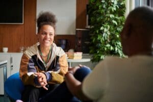 A woman smiles while talking with a therapist in a calm, welcoming office, reflecting a supportive mental health counseling session.