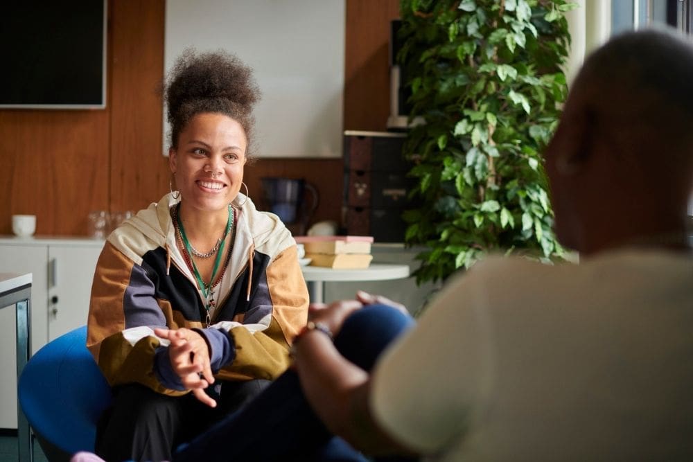 A woman smiles while talking with a therapist in a calm, welcoming office, reflecting a supportive mental health counseling session.