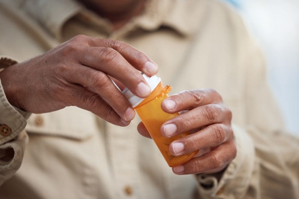 Close-up of hands opening an orange prescription pill bottle.