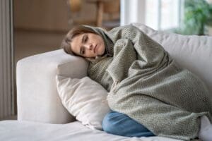 Person wrapped in a patterned gray blanket sitting on a sofa; image used in content discussing the risk of suicide.